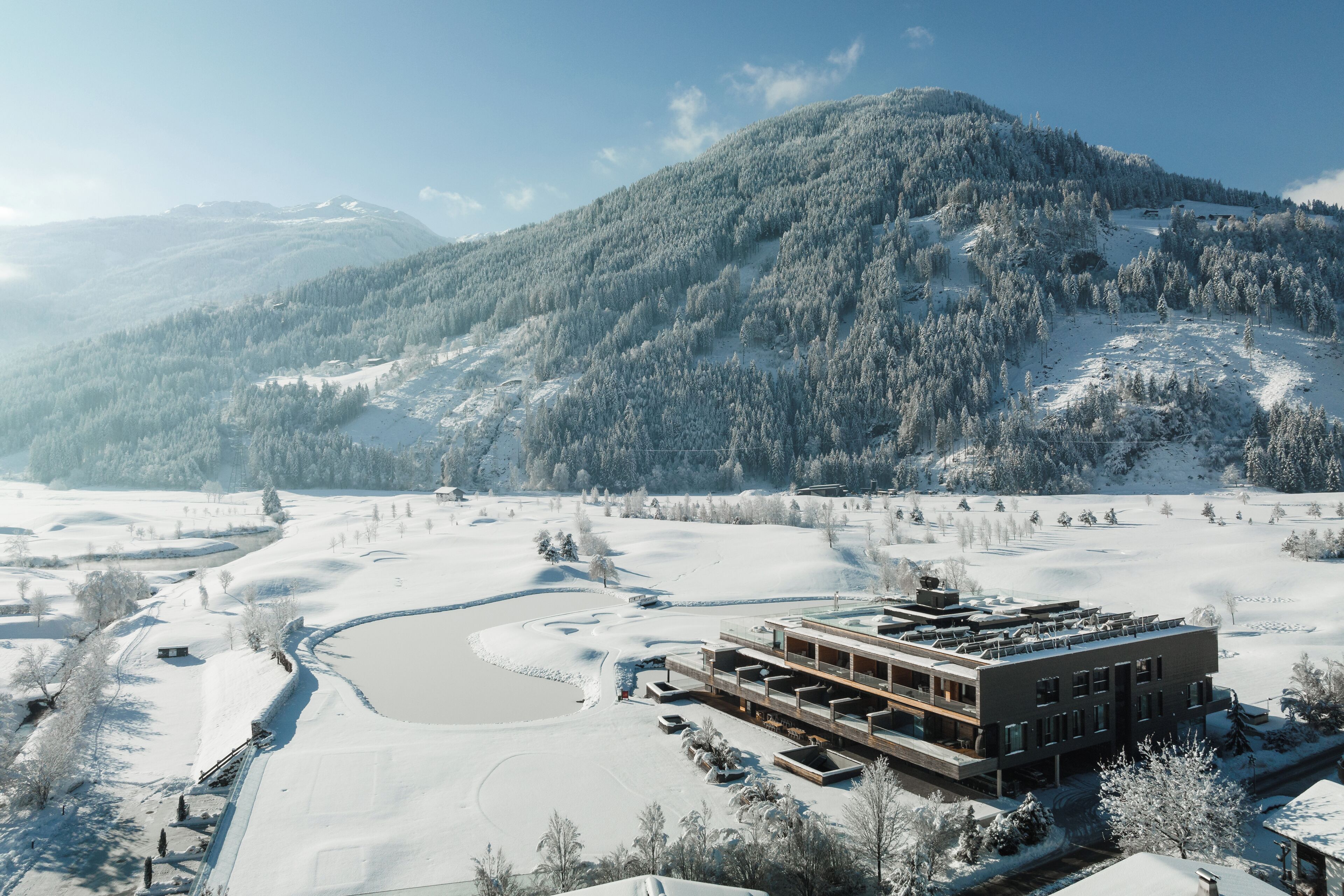 Un edificio moderno de techo plano, rodeado de campos nevados y una montaña al fondo.