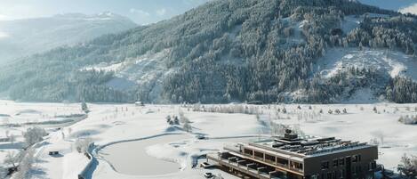 Un edificio moderno de techo plano, rodeado de campos nevados y una montaña al fondo.