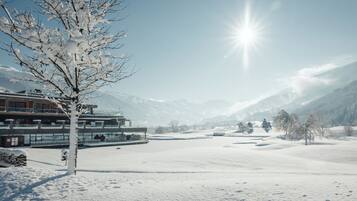 Un paisaje nevado con un edificio que tiene ventanas amplias y un balcón con vista a un campo cubierto de nieve y montañas.