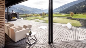 Une terrasse en bois avec des sièges d’extérieur, une cheminée et une vue sur un terrain de golf et des montagnes.