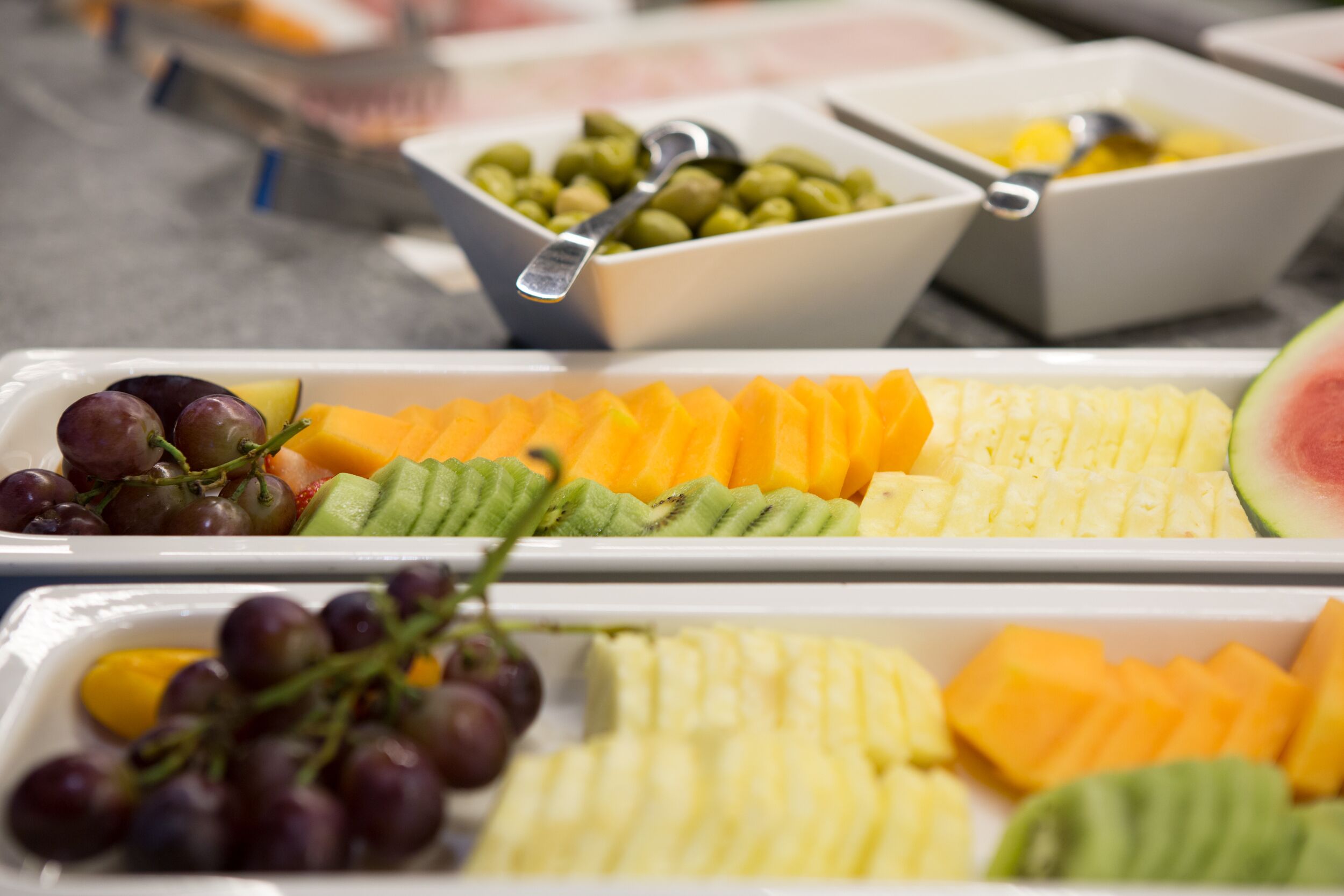 Un bufé con diversas frutas y verduras, incluyendo uvas, kiwi y melón cantalupo.