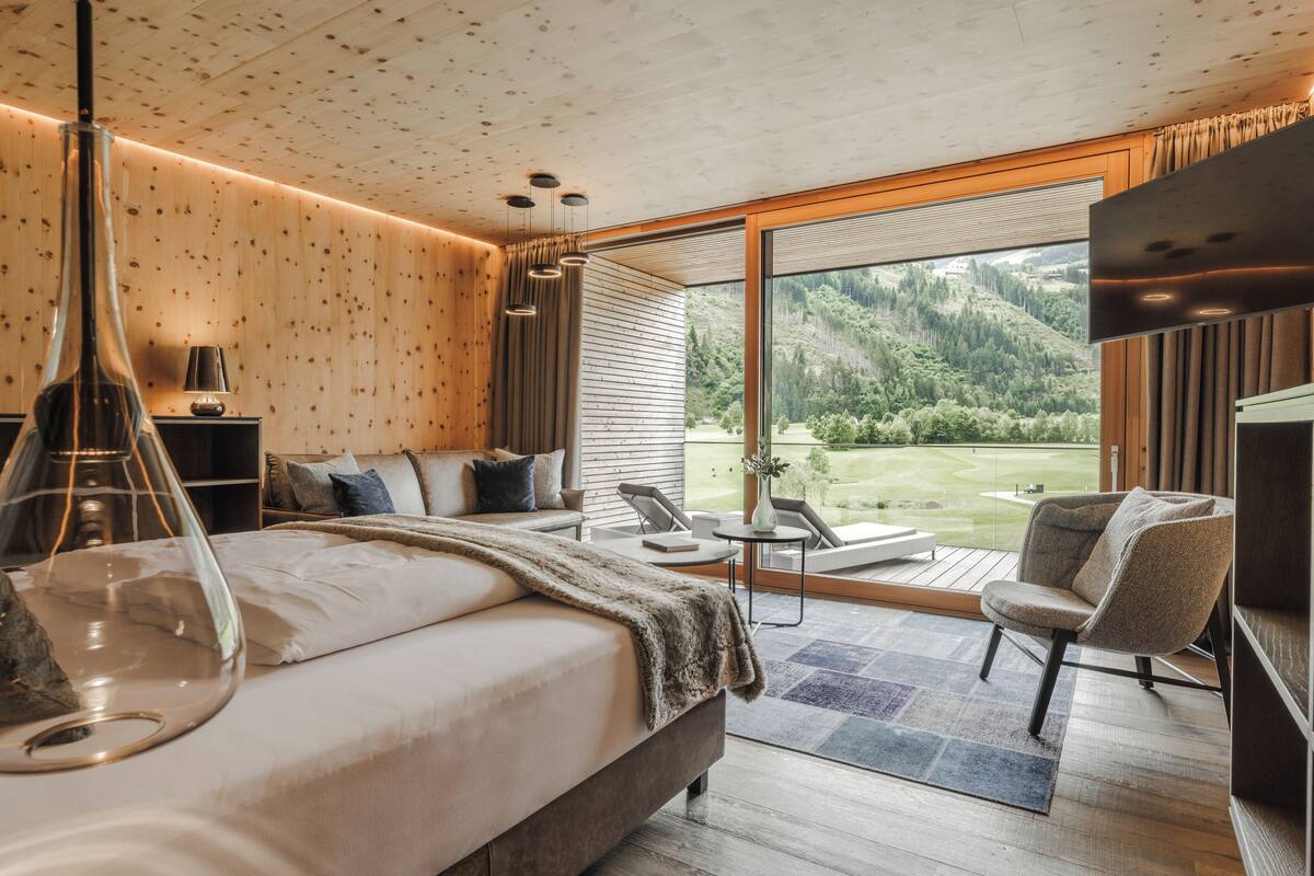 A modern bedroom with a large bed, a seating area with a view of a golf course, and a wooden ceiling.