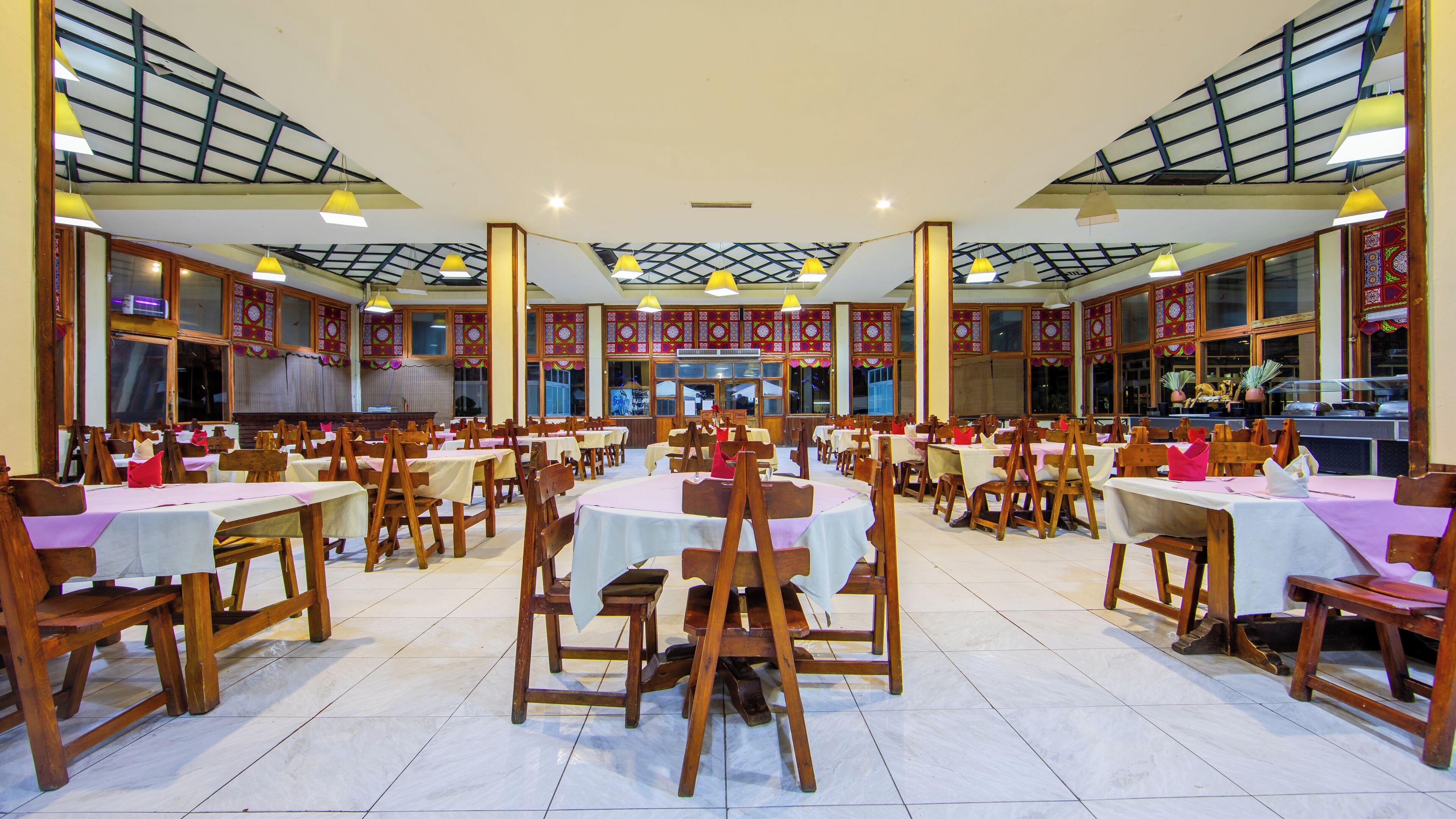 A spacious dining hall with multiple tables and chairs, high ceilings with skylights, and traditional decor.