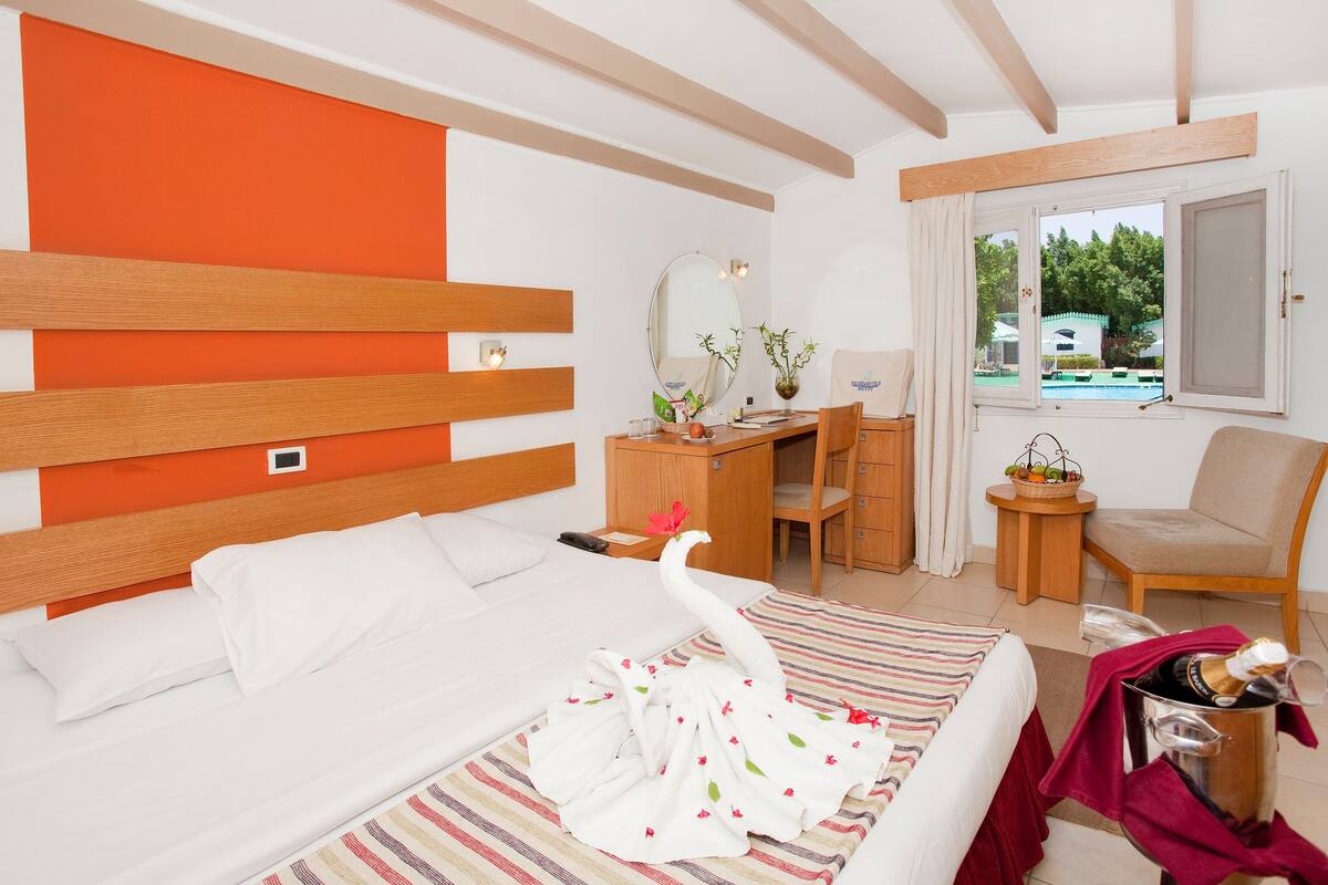 A hotel room with a bed, a desk, a chair, and a view of a pool.