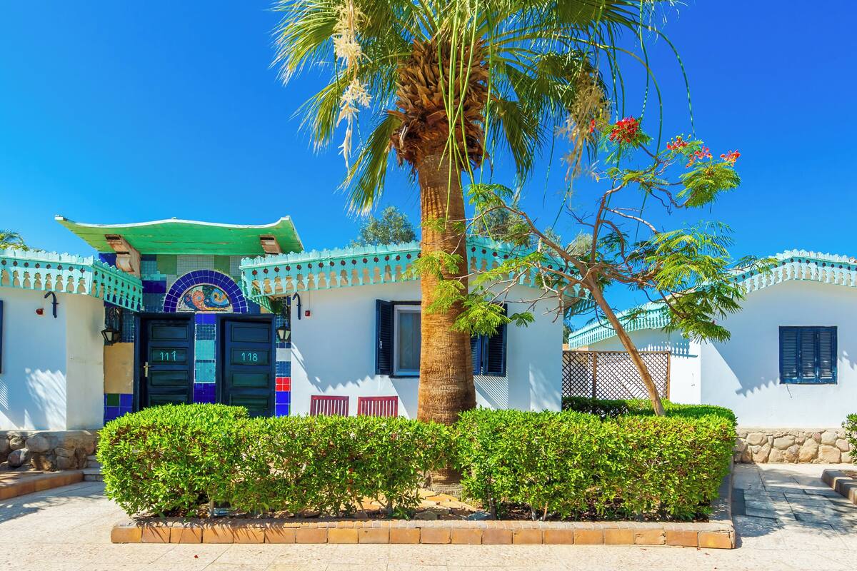 A traditional building with a green roof, two doors, and a palm tree in the foreground.