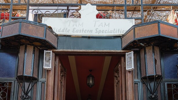 Entrada de um edifício com uma placa indicando 'TAM TAM Middle Eastern Specialty'.