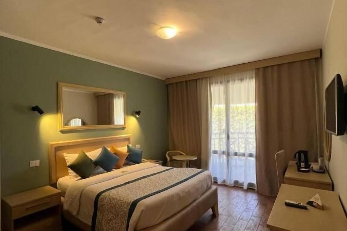 A hotel room with a bed, bedside tables, a desk, a chair, a television, and a window with curtains.