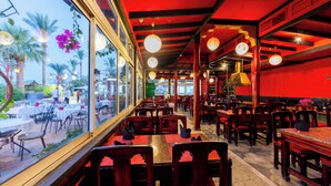 Restaurante interno com mesas e cadeiras de madeira, grandes janelas e luminárias pendentes.