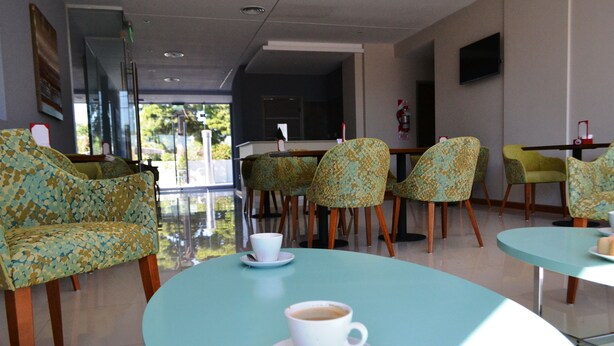 Un área de estar interior moderna con mesas redondas y sillas estampadas, una taza blanca sobre una mesa y un extintor en la pared.