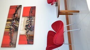 Una habitación con dos cuadros abstractos en la pared, una escalera de madera y una silla roja.