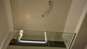 Un baño moderno con cabina de ducha de vidrio, barra de apoyo visible y suelo de baldosas.