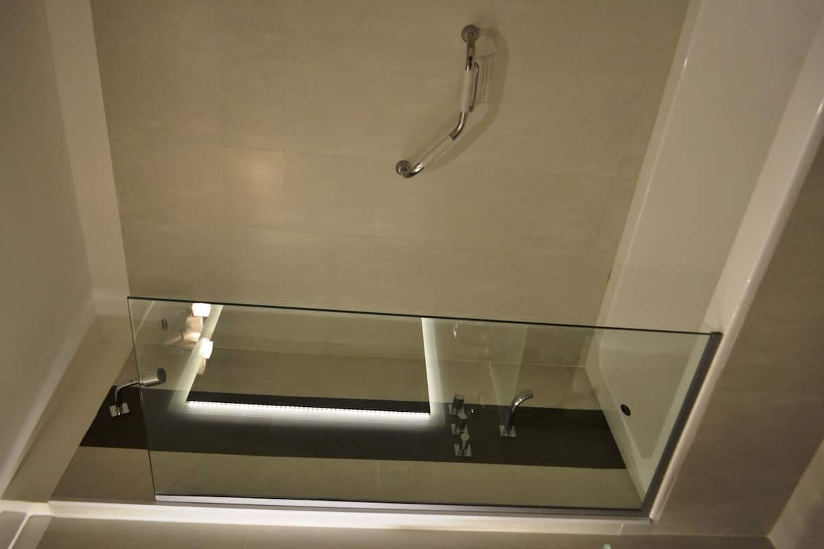 A modern bathroom with a glass shower enclosure, a visible handrail, and a tiled floor.
