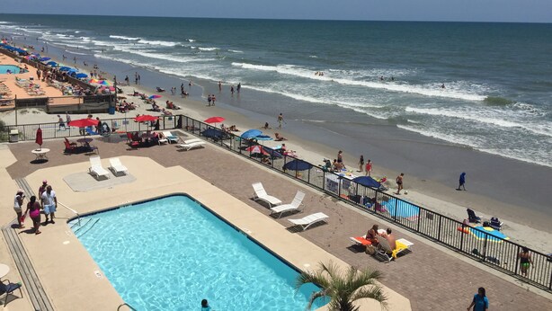 Un hôtel situé en bord de mer, doté d’une piscine, de chaises longues et de parasols.