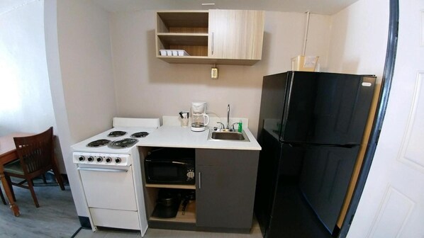 A compact kitchenette with a stove, oven, sink, and a black refrigerator. - Garden City Inn (Murrells Inlet)