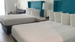 Une chambre d’hôtel avec deux lits, une table de chevet avec une lampe, un canapé et une fenêtre avec des rideaux.