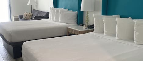 A hotel room with two beds, a nightstand with a lamp, a sofa, and a window with curtains.
