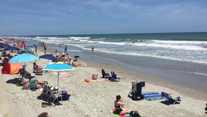 Une plage où l’on peut voir des gens bronzer et se baigner, ainsi que des parasols et des chaises de plage.