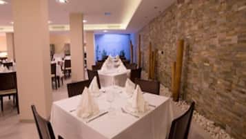 Un restaurant avec des tables dressées pour le service, un mur en pierre et une vue sur l’intérieur.