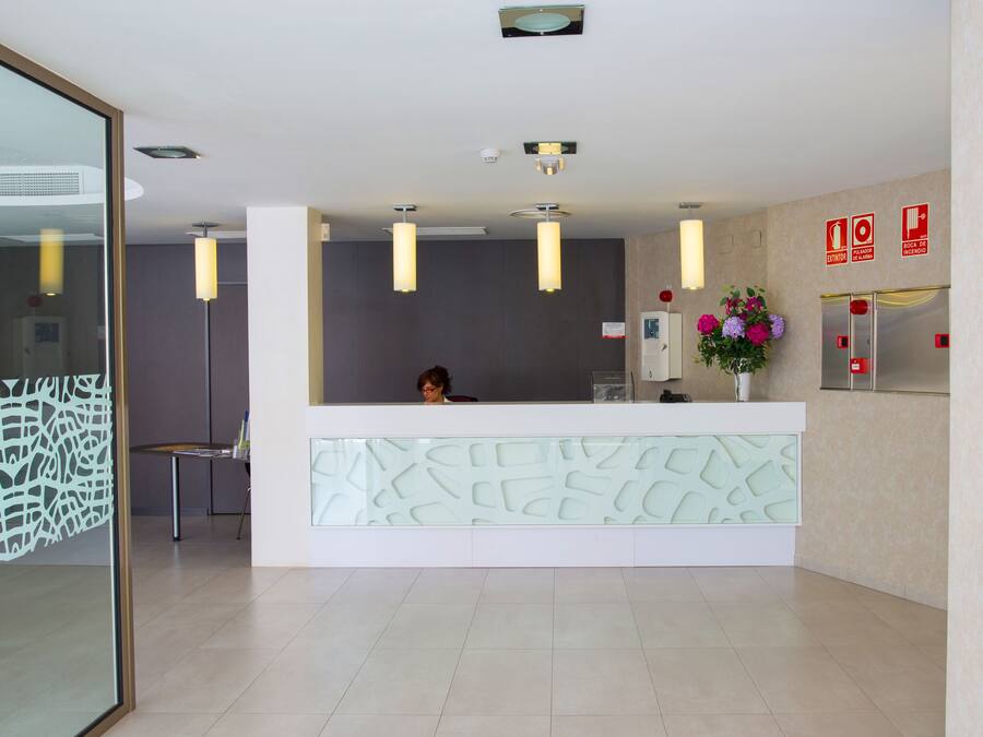 Un área de recepción con diseño moderno, que incluye un mostrador de recepción, un detector de incendios instalado en la pared y un arreglo floral decorativo.