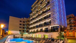 Un hotel de varios pisos con área de piscina, mobiliario exterior y una fachada distintiva.