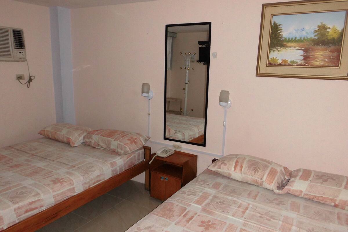 A bedroom with two single beds, a wooden nightstand, a mirror, and a wall-mounted lamp.