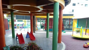 A playground with slides and a rotating play structure, surrounded by colorful pillars and a paved area. - Hotel Francisco II (Salinas)