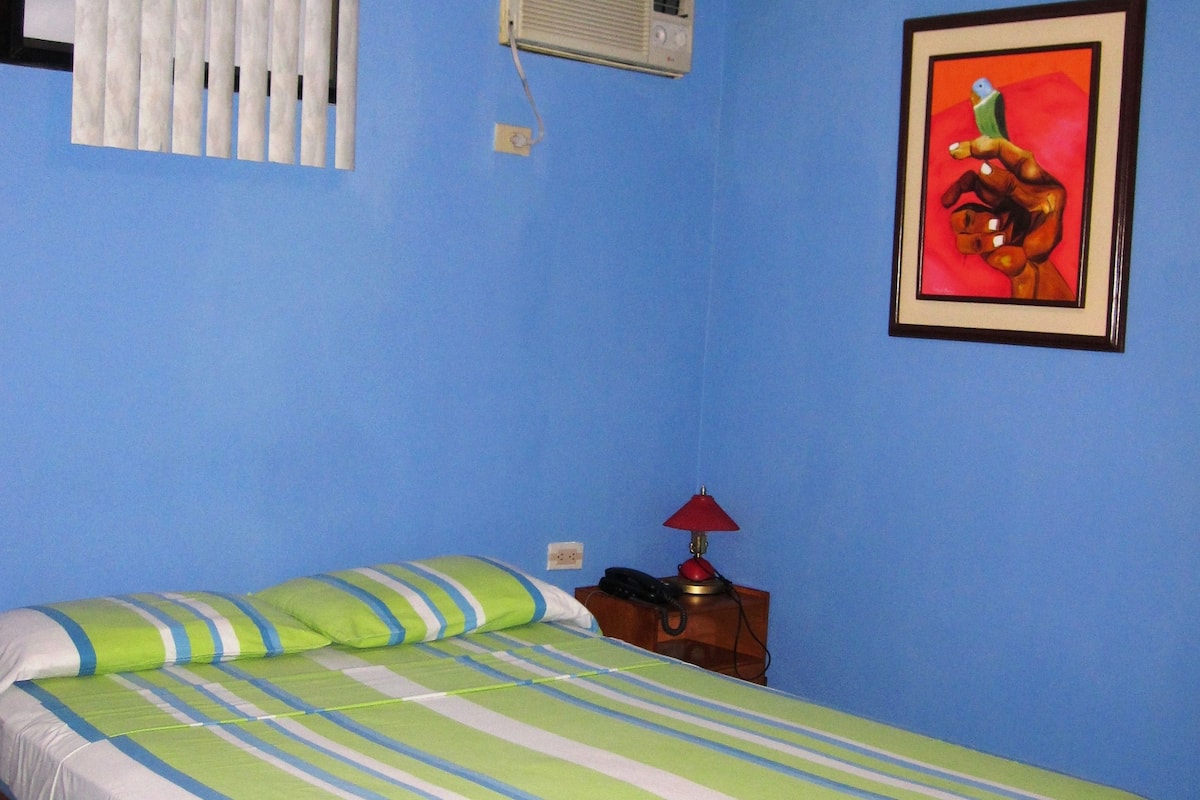 A room with a bed, a nightstand, a lamp, a framed picture, and an air conditioning unit.