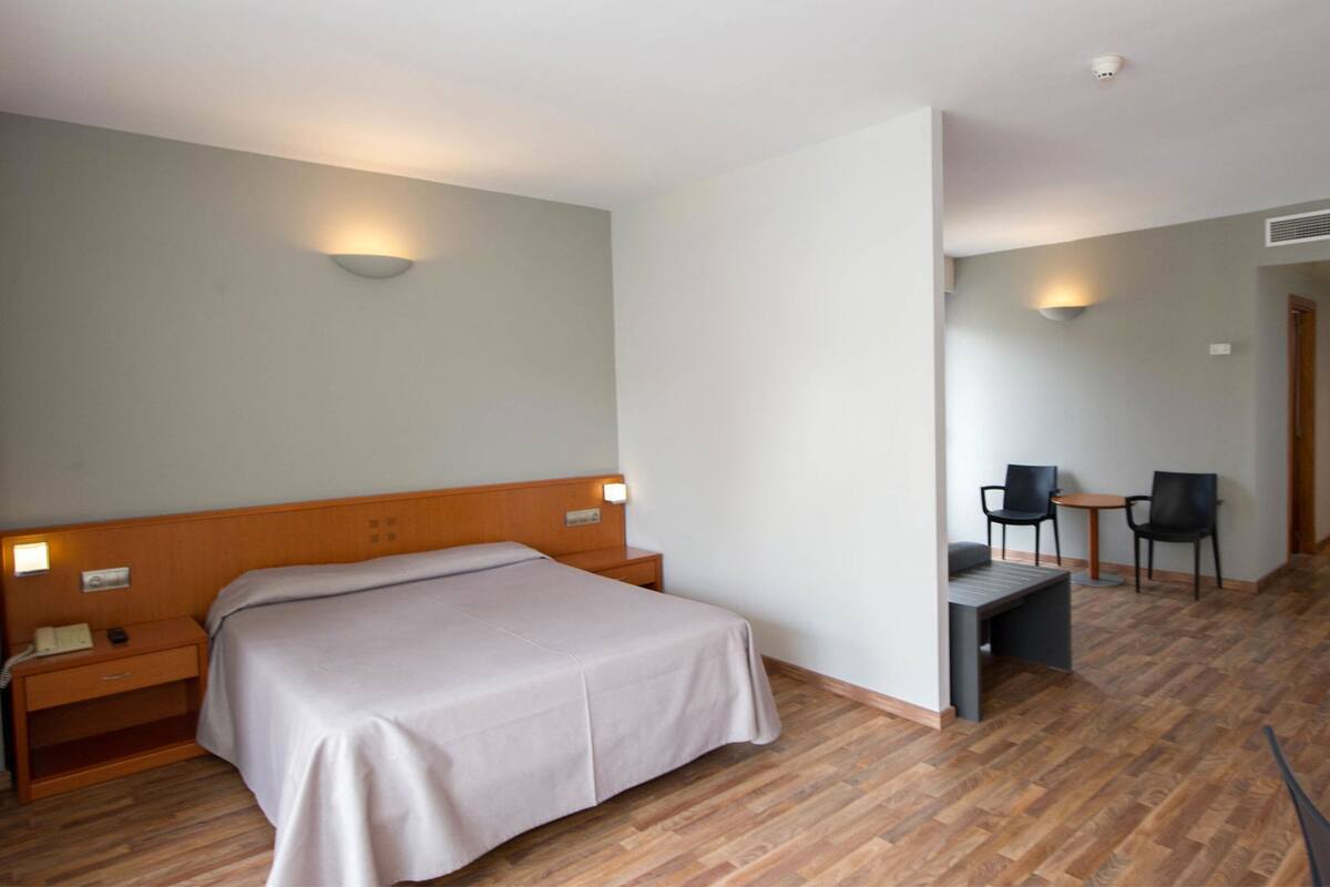 Una habitación de hotel con cama, mesita de noche, lámpara y un escritorio con dos sillas.