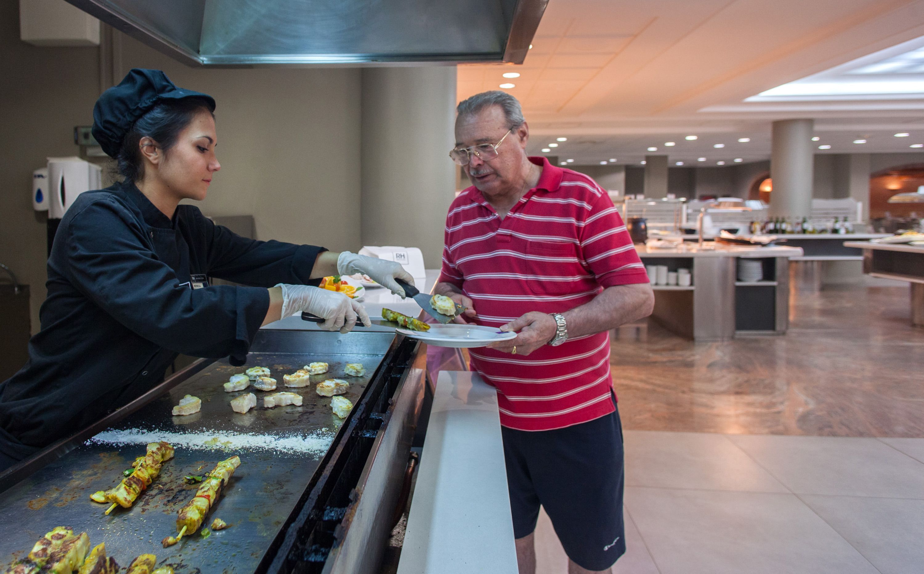 Zona de buffet con una parrilla, personal de servicio y un hombre con camisa a rayas.