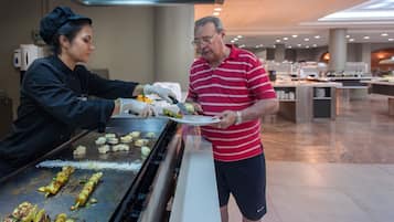 Zona de buffet con una parrilla, personal de servicio y un hombre con camisa a rayas.