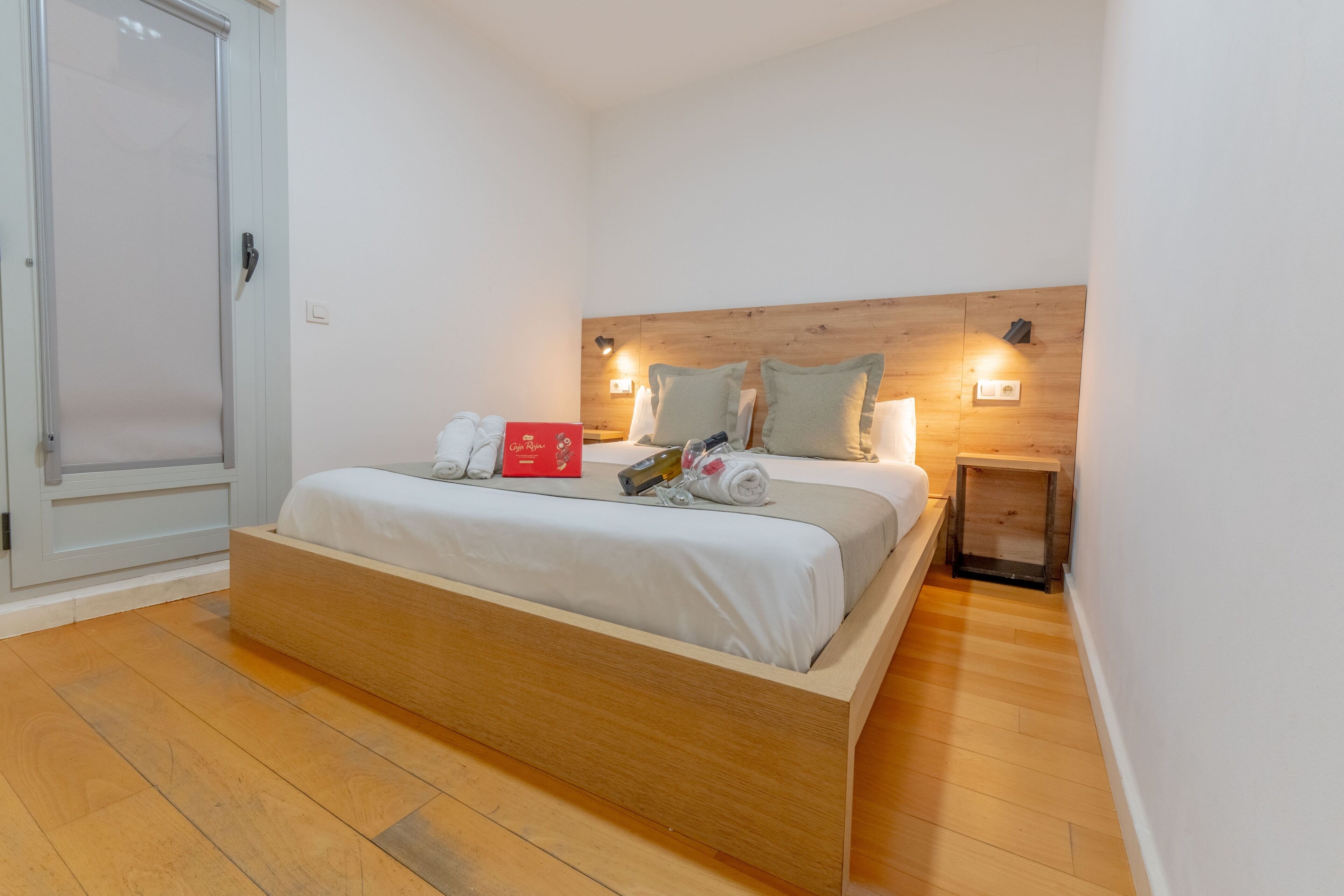 Quarto com estrutura de cama de madeira, mesa de cabeceira e luminária na parede.