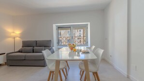 A dining area with a white table, four chairs, a grey sofa, and a floor lamp. - Apartamentos Santa Faz by Be Alicante (Alicante)