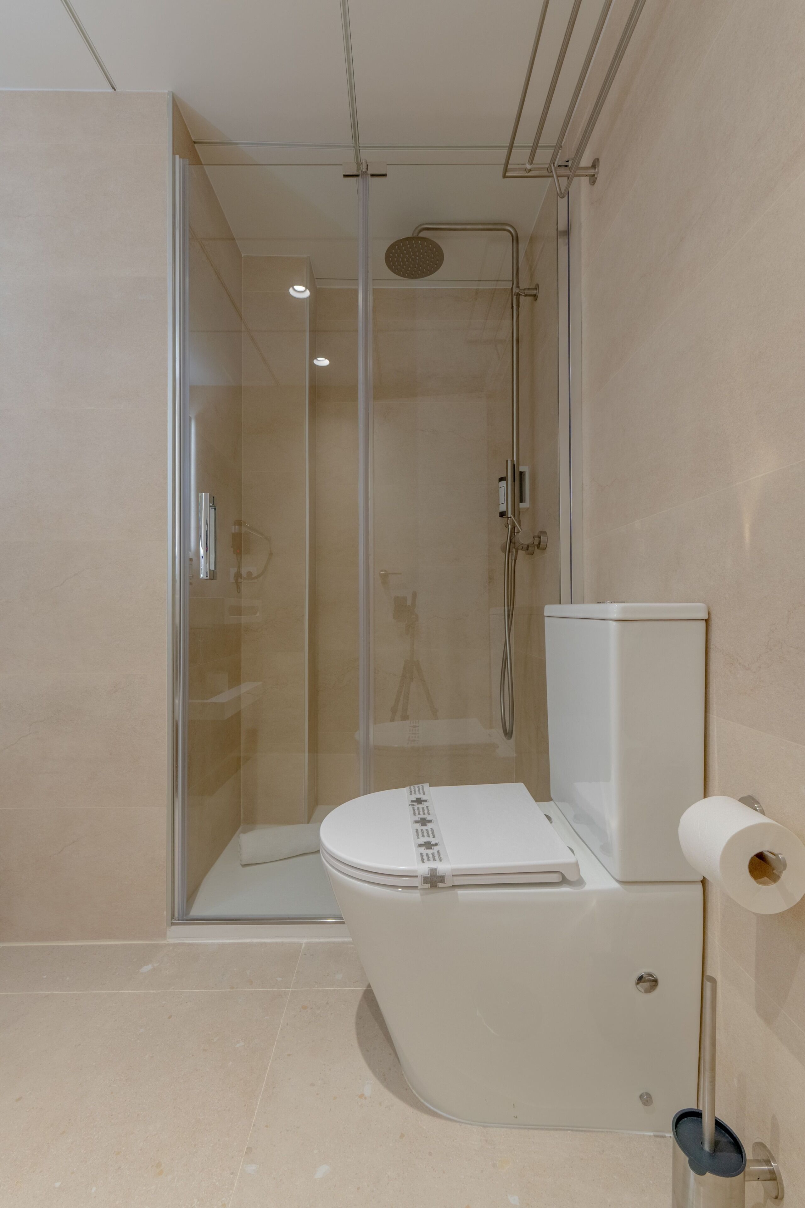 Un baño moderno con ducha envuelta en vidrio, un inodoro blanco y un dispensador de papel higiénico a la vista.