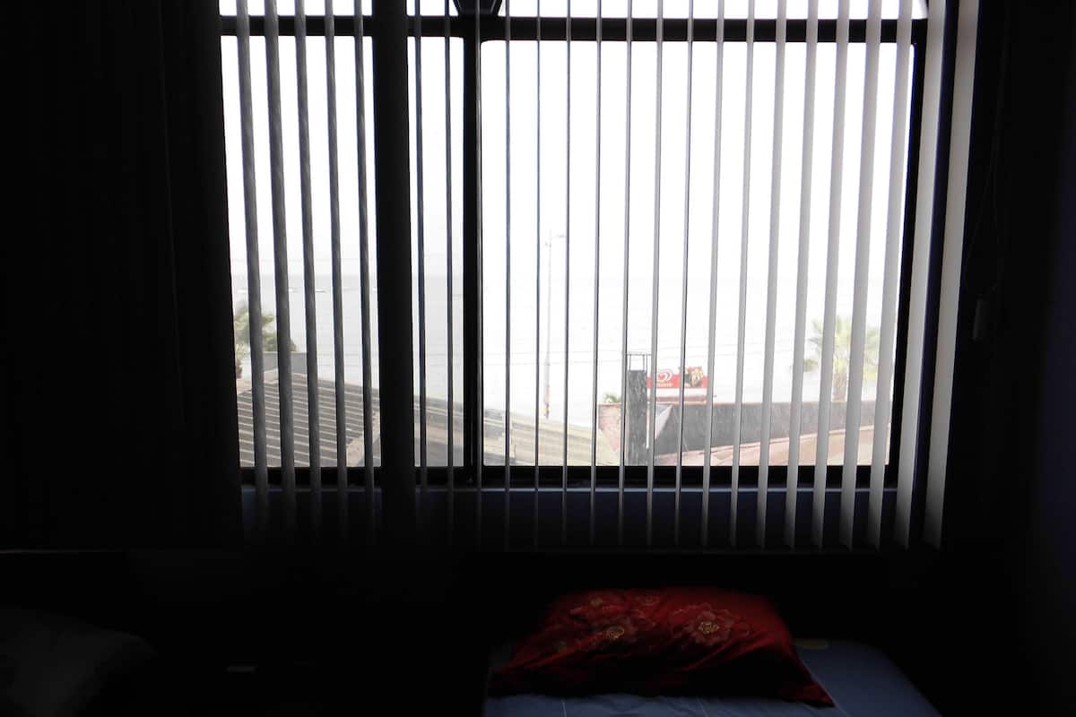 Una habitación con cama, ventana con persianas verticales y vista a la calle.