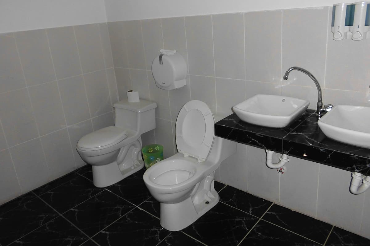 Baño con dos inodoros, un lavabo y dispensador de papel higiénico.