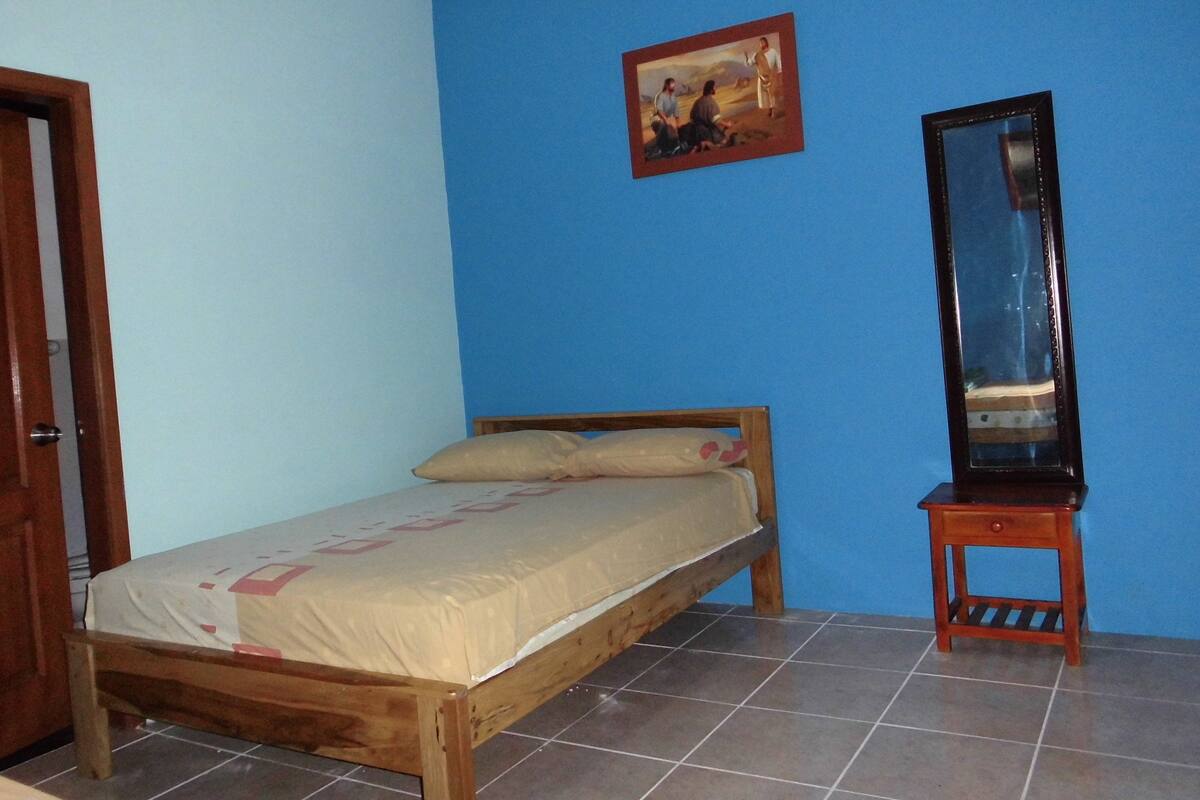 Un dormitorio con cama de madera, una mesita de noche pequeña, un espejo y un cuadro en la pared.