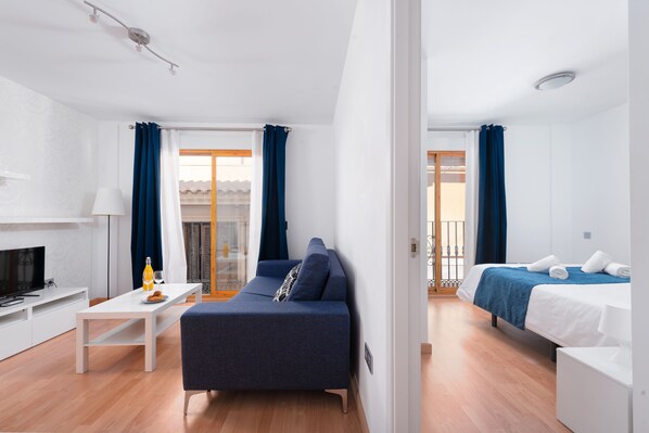 A modern hotel room with a sofa, a bed, a TV, and a dining area.