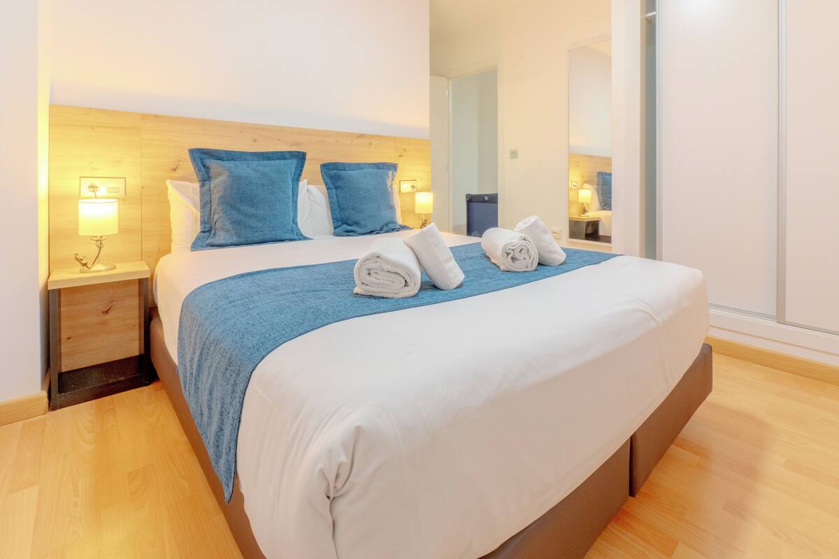 A hotel room with a large bed, two nightstands with lamps, a wooden headboard, and a mirror.