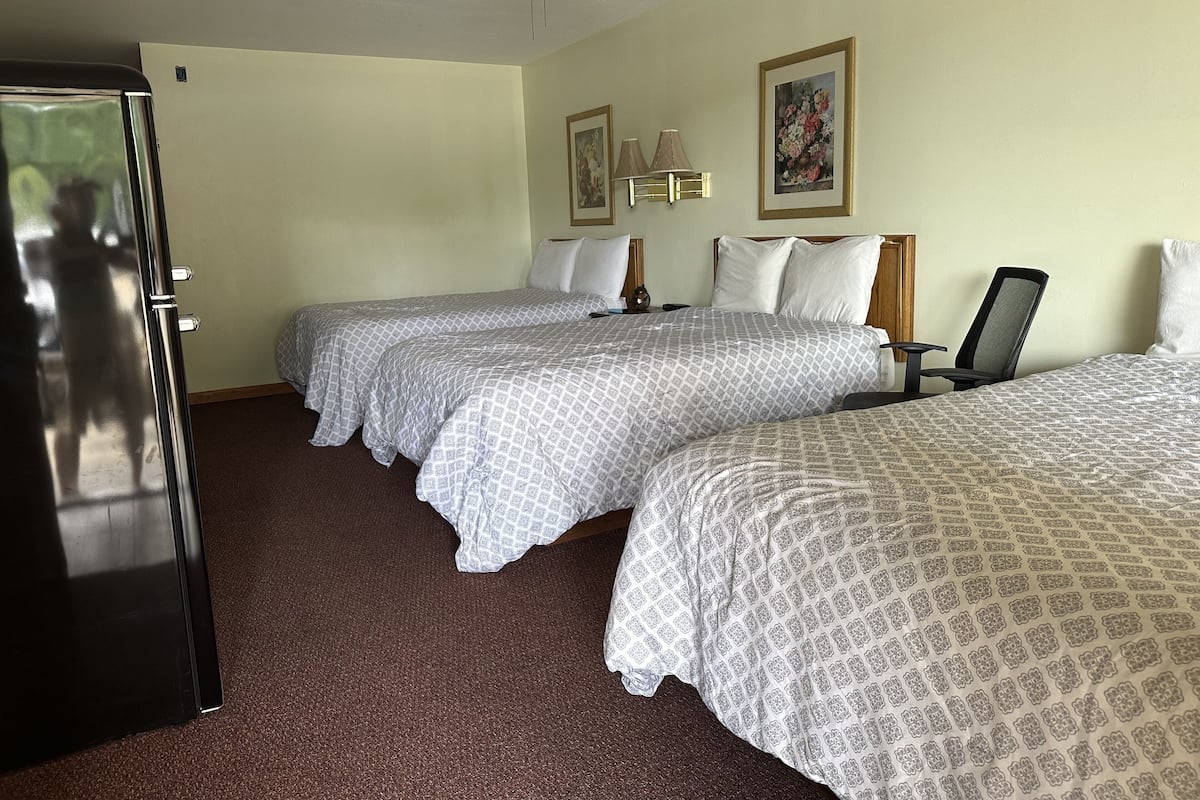Une chambre d’hôtel avec trois lits, un ventilateur de plafond, une porte et deux lampes fixées au mur.
