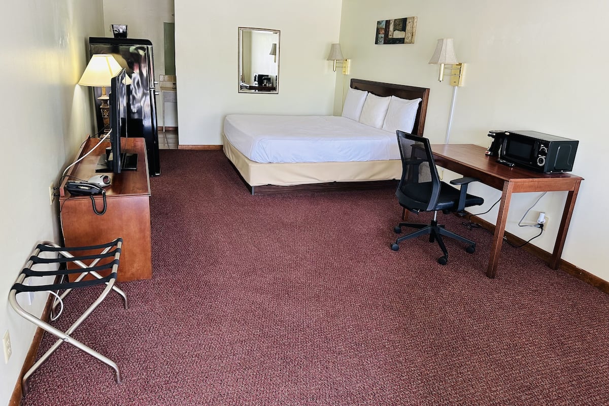 Une chambre d’hôtel équipée d’un lit, d’un bureau, d’une chaise, d’une lampe de bureau et d’un four à micro-ondes.