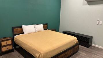 A bed with a wooden frame and a beige bedspread, a bedside table with a woven basket, and a wall-mounted air conditioner.