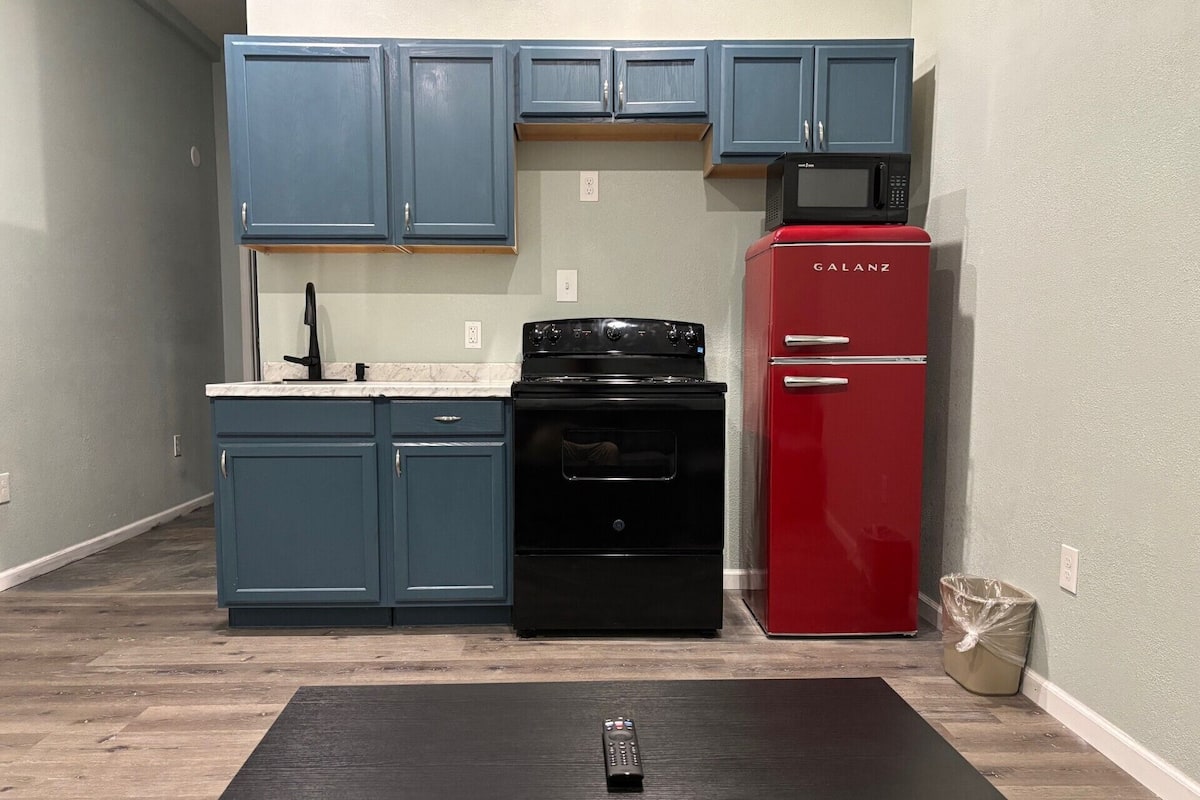 Une cuisine de taille réduite avec des meubles bleus, une cuisinière noire et un réfrigérateur rouge.