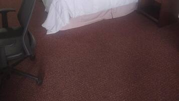 A hotel room with two single beds, a desk, a chair, and a lamp.