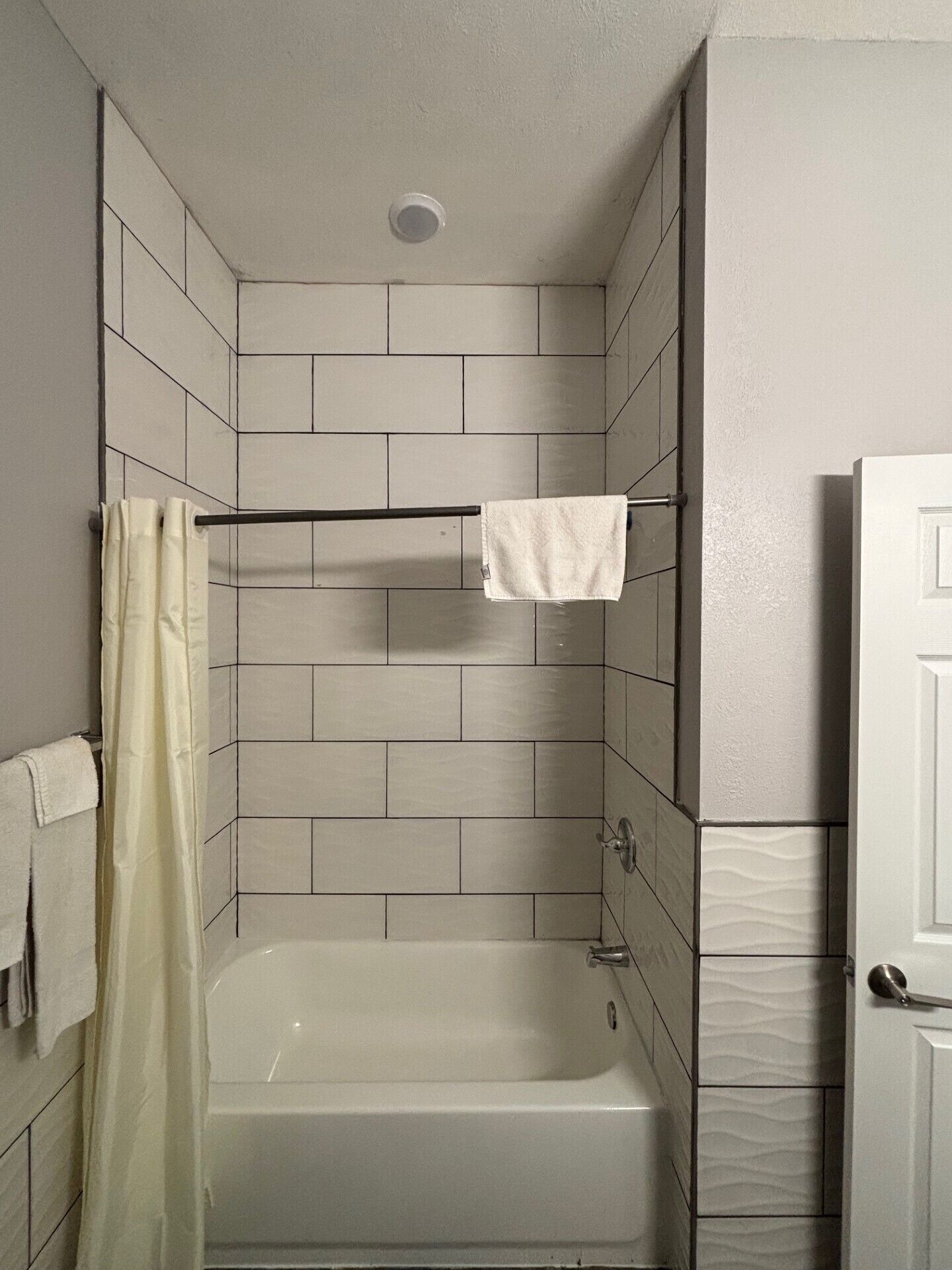 Een badkamer met een bad, betegelde wanden, een douchegordijn en een handdoekrek.
