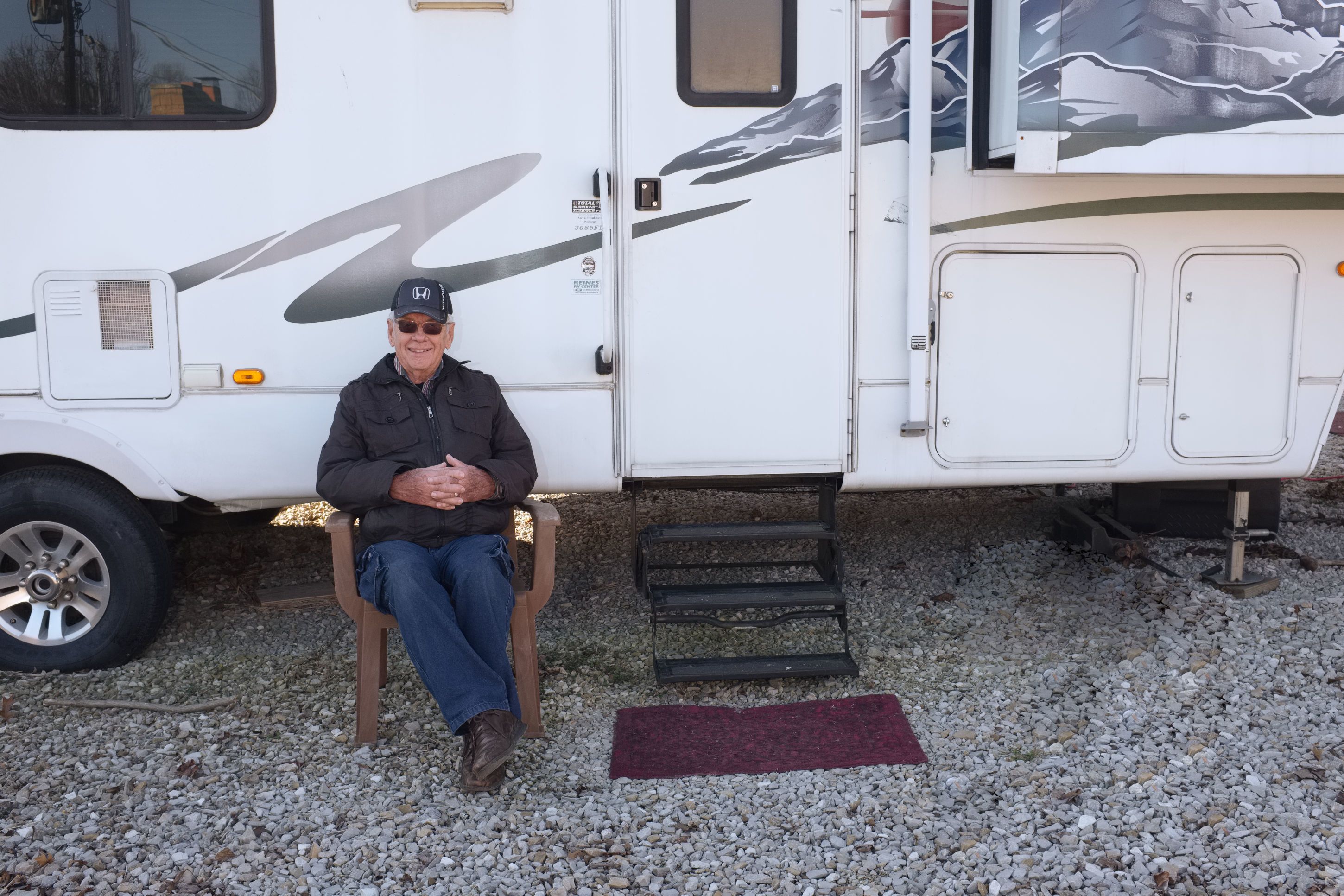 A person seated on a chair next to a white RV with a step leading up to the door.
