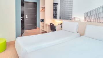 A hotel room with a bed, a desk, a chair, a wardrobe, and a view of a modern building.