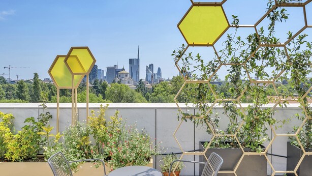 Terraza en la azotea con vistas a un horizonte urbano, macetas hexagonales con plantas, y sillas y mesas de metal.