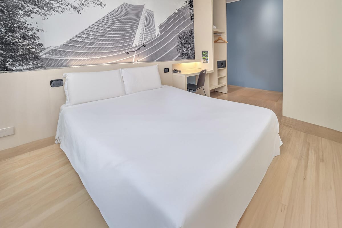 A hotel room with a bed, a desk, and a wall-mounted TV.