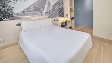 Una habitación de hotel con cama, escritorio y televisor montado en la pared.