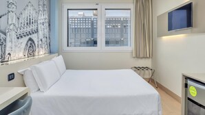 Habitación de hotel con una cama grande, un escritorio, una silla, un televisor montado en la pared y una ventana con cortinas.